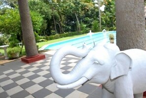 A large elephant statue in a landscaped area with a pool and trees.