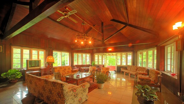 A spacious living room with wooden beams, large windows, and floral-patterned furniture. - The Bungalow at Pantiya Estate (Matugama)