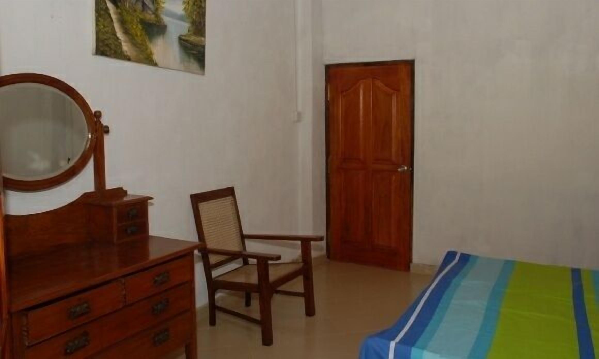 Un dormitorio con un aparador de madera, una silla, una cama con colcha a rayas y una puerta de madera.