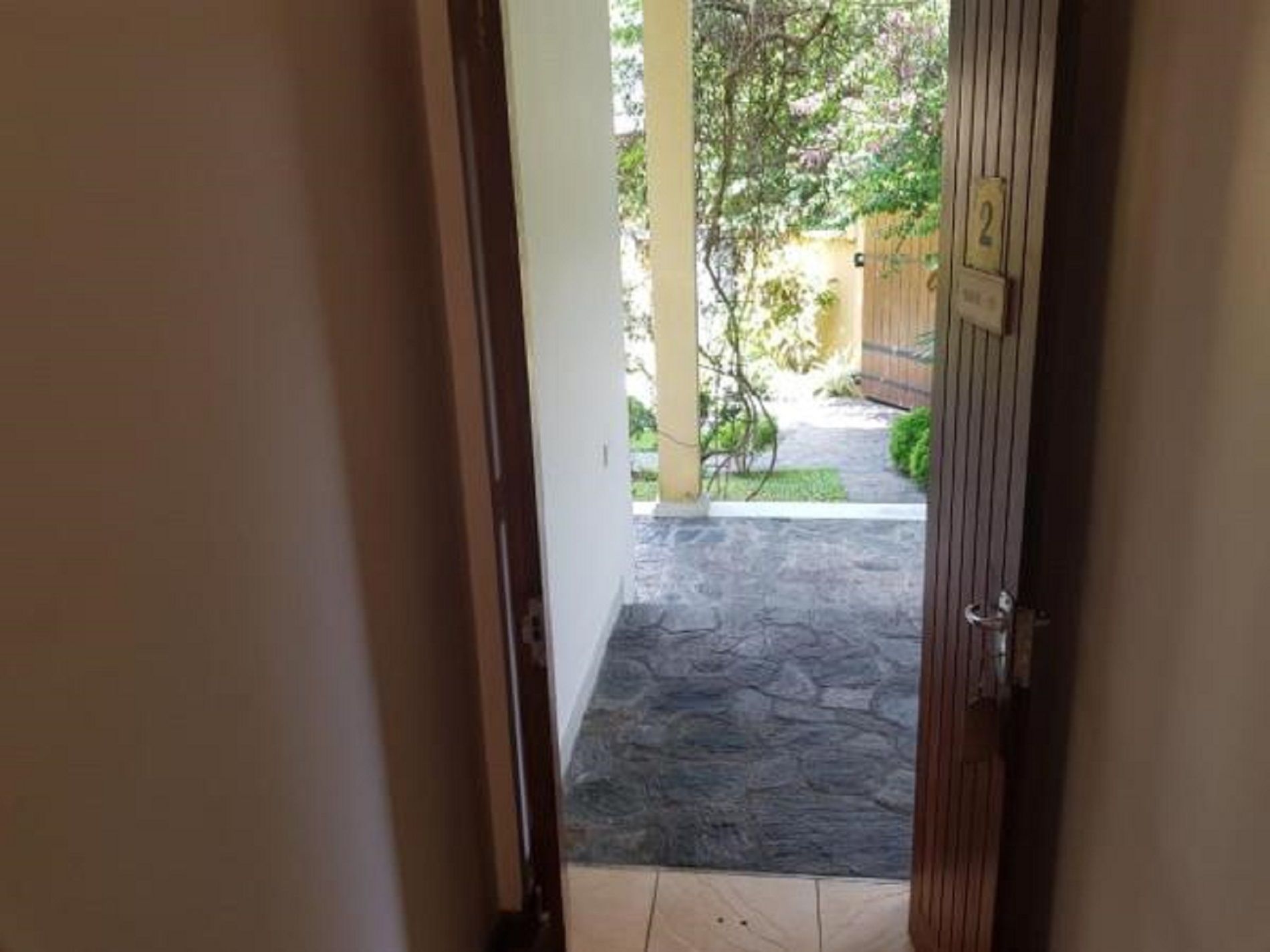 Vista a través de una puerta a un patio con sendero de piedra, cerca de madera y follaje.