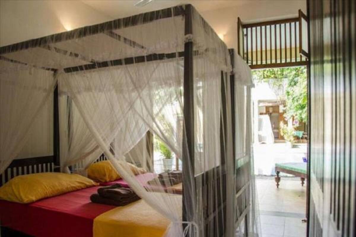 A room with a bed covered by a mosquito net, a red bedspread, and a yellow pillow.