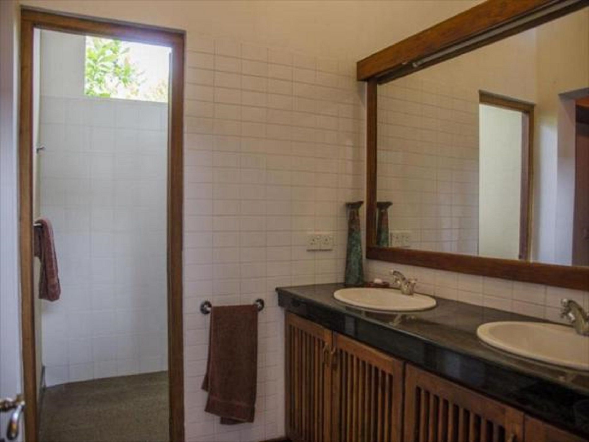 A bathroom with a wooden vanity, two sinks, a large mirror, and a towel hanging on the wall.
