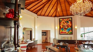 Un vaste espace dédié à la salle à manger, avec des tables et des chaises en bois, un lustre et un grand tableau coloré accroché au mur.