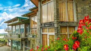 Un immeuble en pierre à plusieurs étages, doté de grandes fenêtres et de balcons, entouré d’une végétation luxuriante et de fleurs.