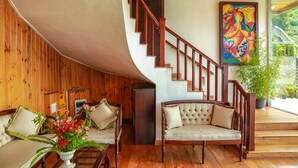 Un intérieur en bois avec un plafond incurvé, un escalier avec des rampes en bois, un canapé avec des coussins, une plante en pot et une peinture abstraite aux couleurs vives accrochée au mur.