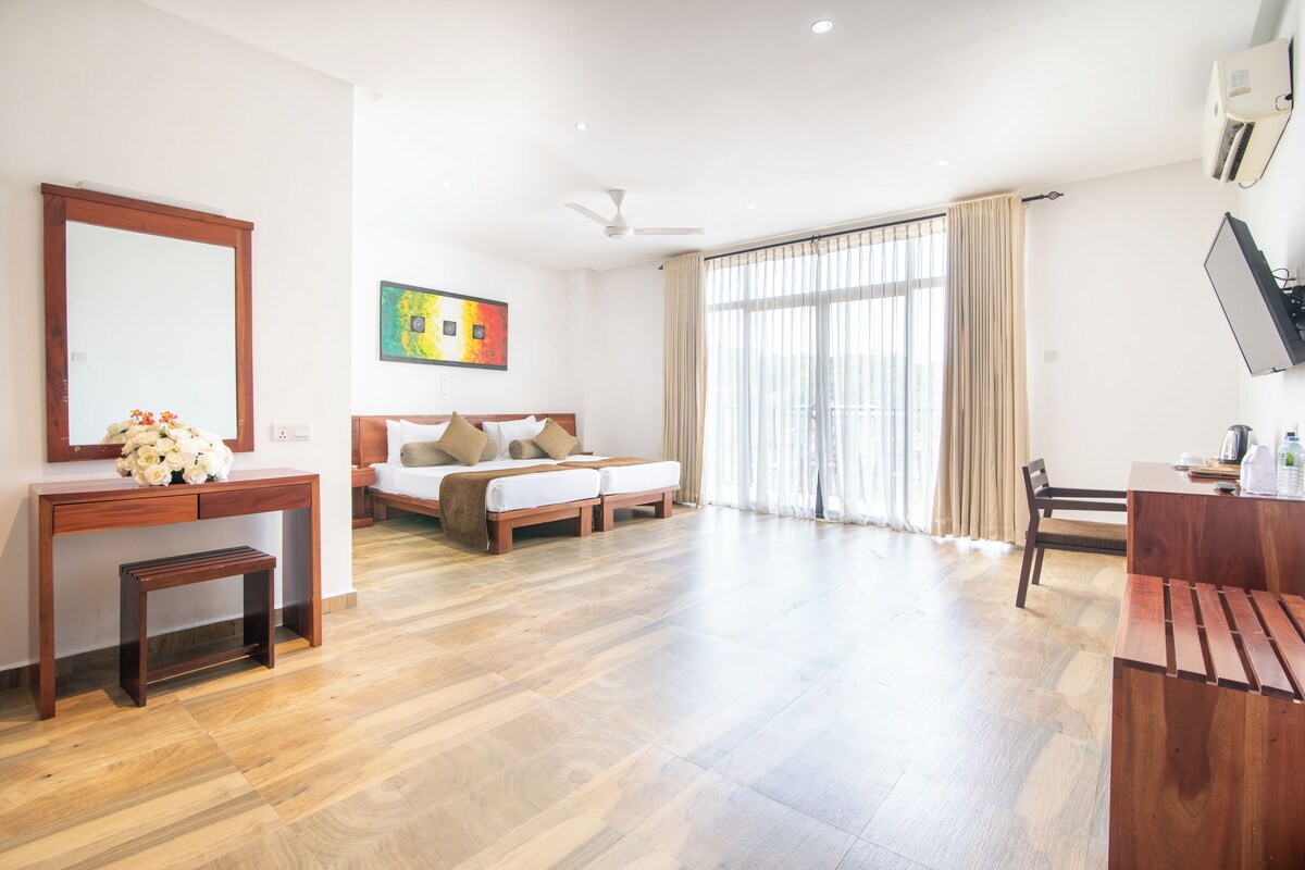 A spacious hotel room with a bed, a desk, a chair, a small table, and a large window with curtains.