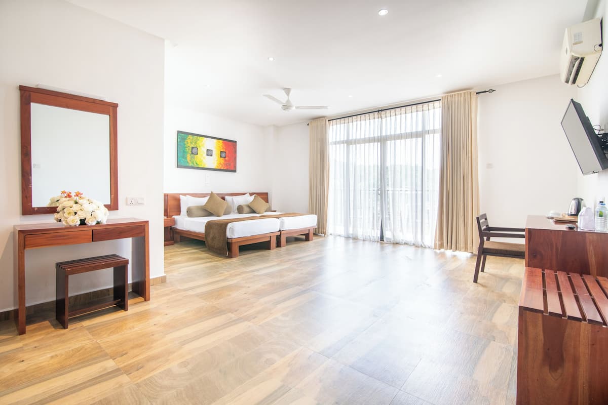 A spacious hotel room with a bed, a desk, a chair, a small table, and a large window with curtains.