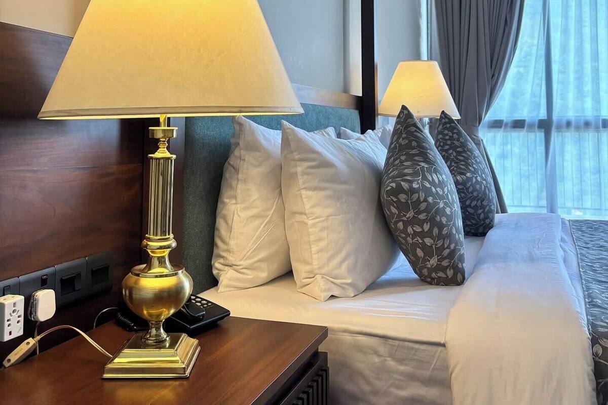 Ein Hotelzimmer mit einem Bett, einem Nachttisch mit Lampe, einer Fernbedienung und einer Steckdose.
