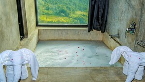 A bathroom with a bathtub, a window with a view of a green landscape, and two towels on the floor. - Oak Ray Tea Bush (Kotmale)
