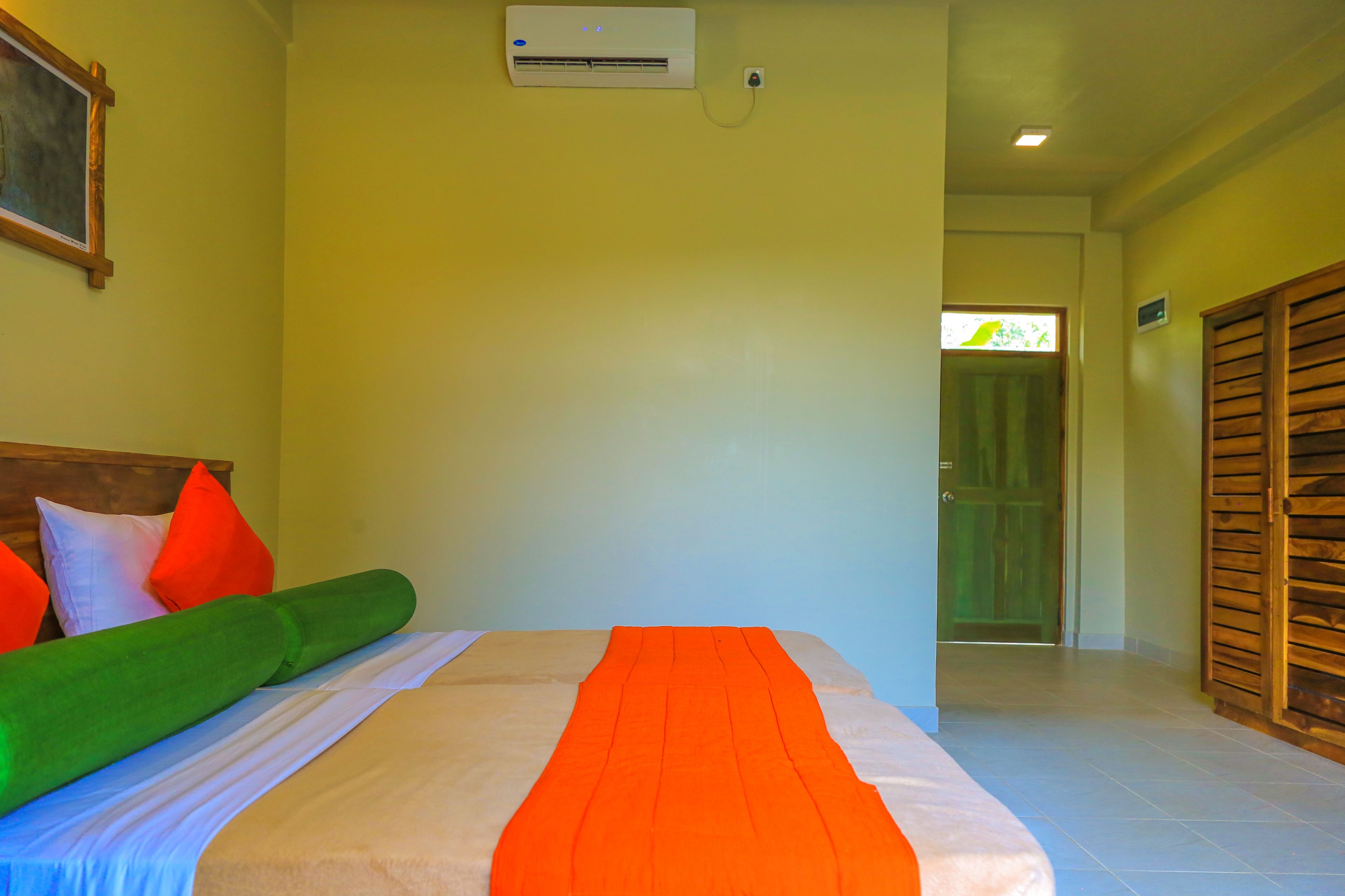 A hotel room with a bed, pillows, a green blanket, and a wooden wardrobe.