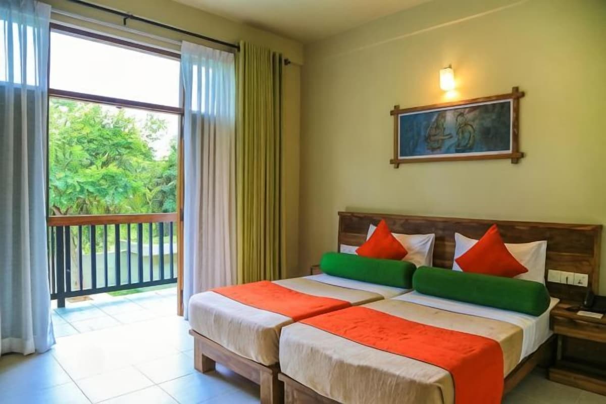 Una habitación de hotel con dos camas, un balcón, un cuadro en la pared y una mesita de noche.