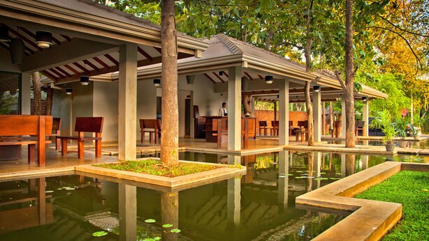 A tranquil outdoor seating area with wooden benches and a central water feature. - Fresco Water Villa (Sigiriya)