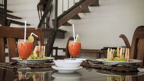 A dining table with two plates of food and two glasses of a red beverage, set in a room with a staircase in the background. - Fresco Water Villa (Sigiriya)