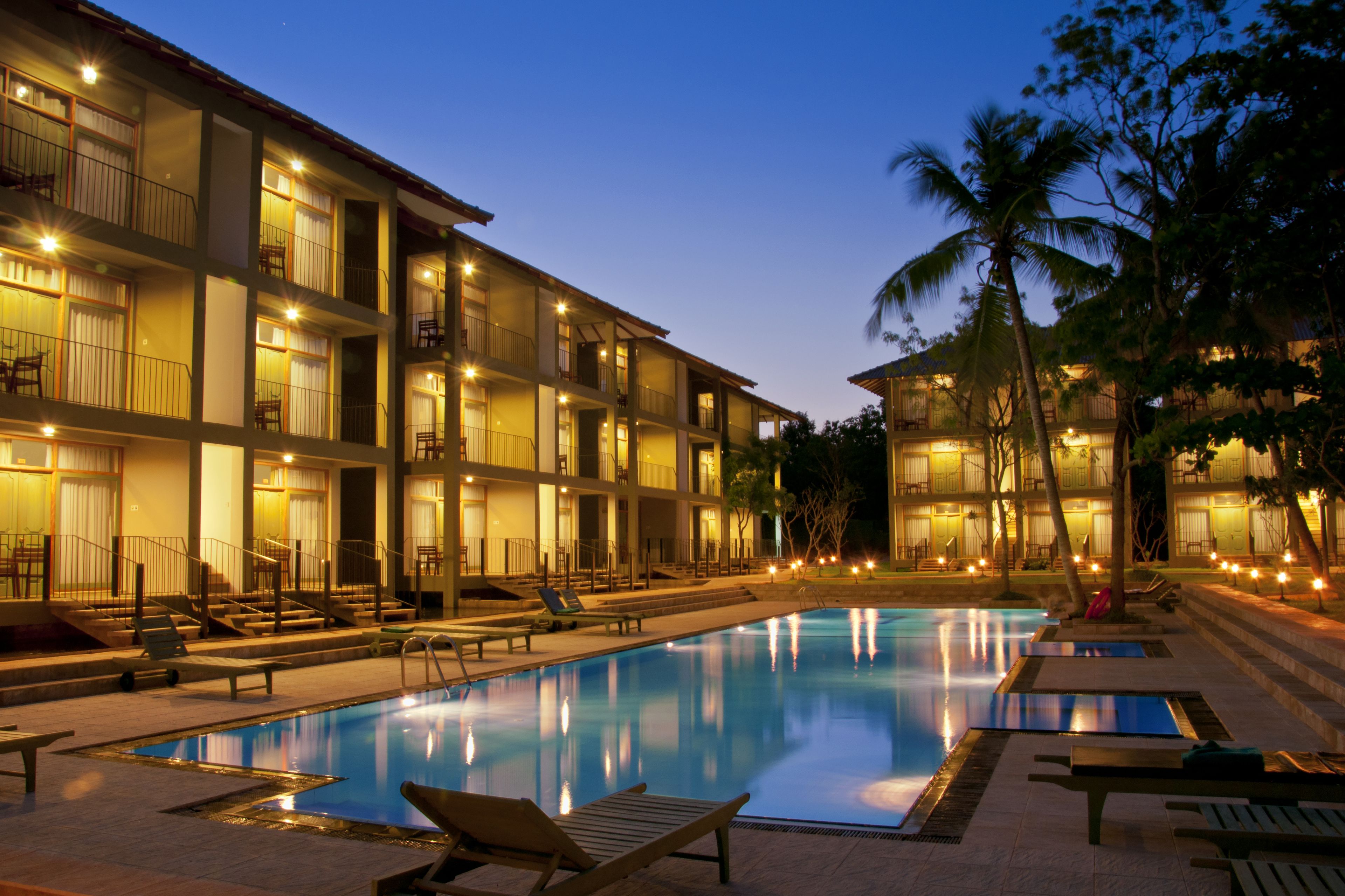 A hotel with a swimming pool, multiple balconies, and palm trees.