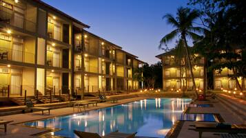 A hotel with a swimming pool, multiple balconies, and palm trees.