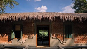 A building with a thatched roof, brick walls, and a central entrance with steps leading up to it. - Fresco Water Villa (Sigiriya)