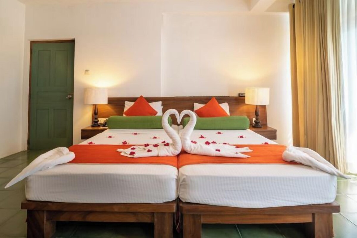 Una cama doble con una disposición de toallas en forma de corazón, dos mesitas de noche con lámparas y una puerta verde.