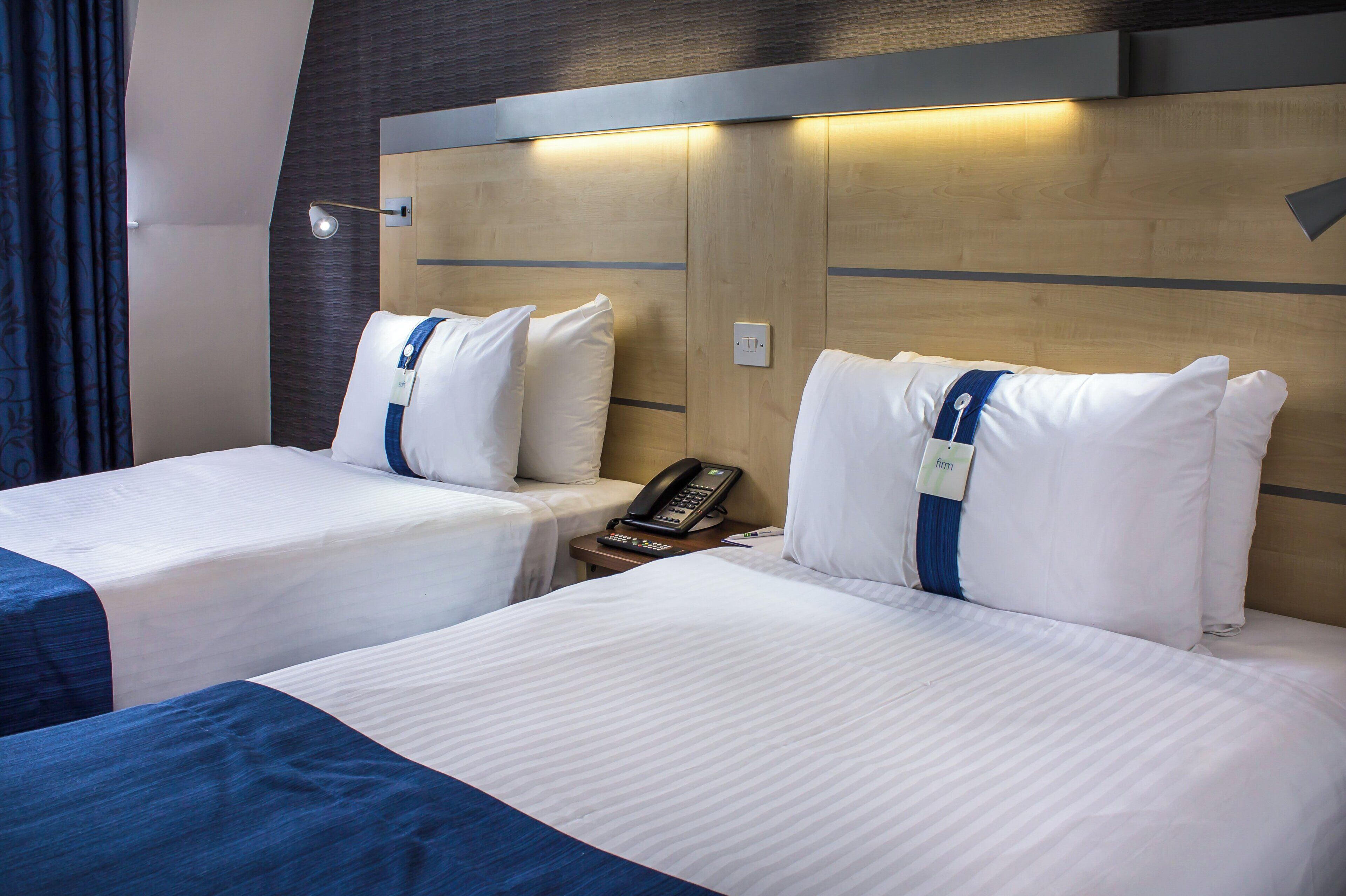 A hotel room with two beds, a bedside table with a phone, and a wall-mounted light.