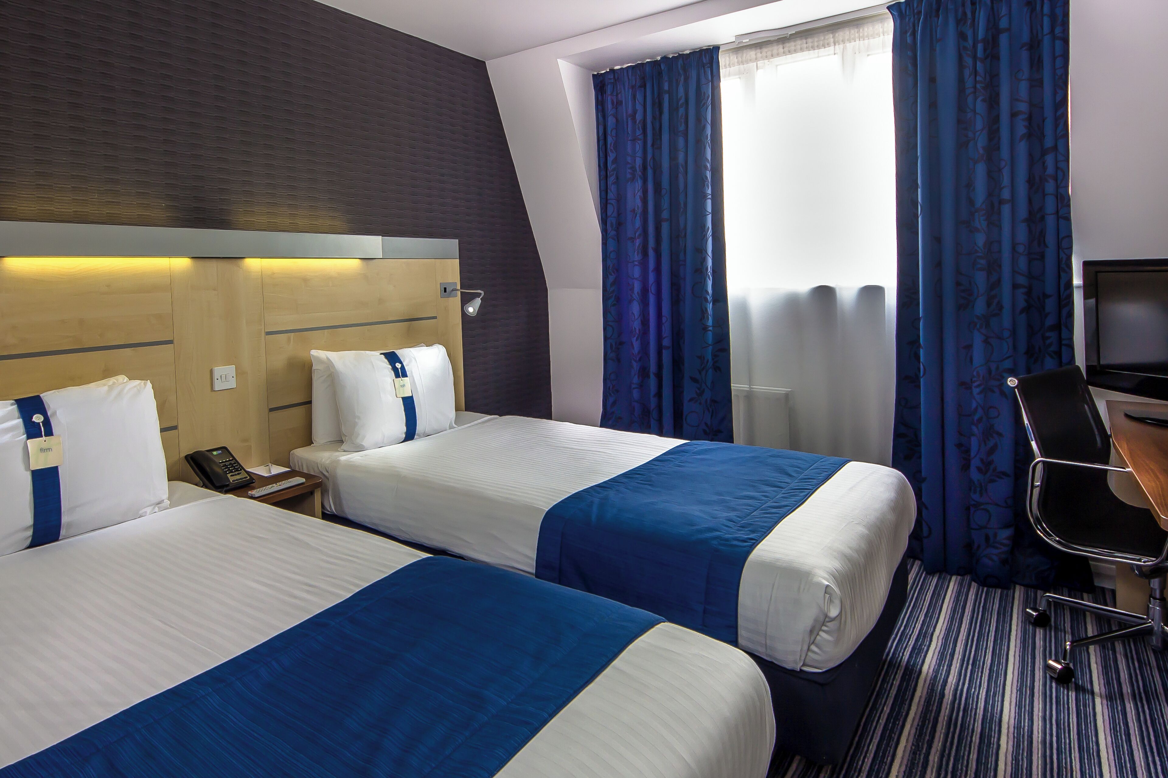 Habitación de hotel con dos camas, un escritorio, una silla y un televisor.