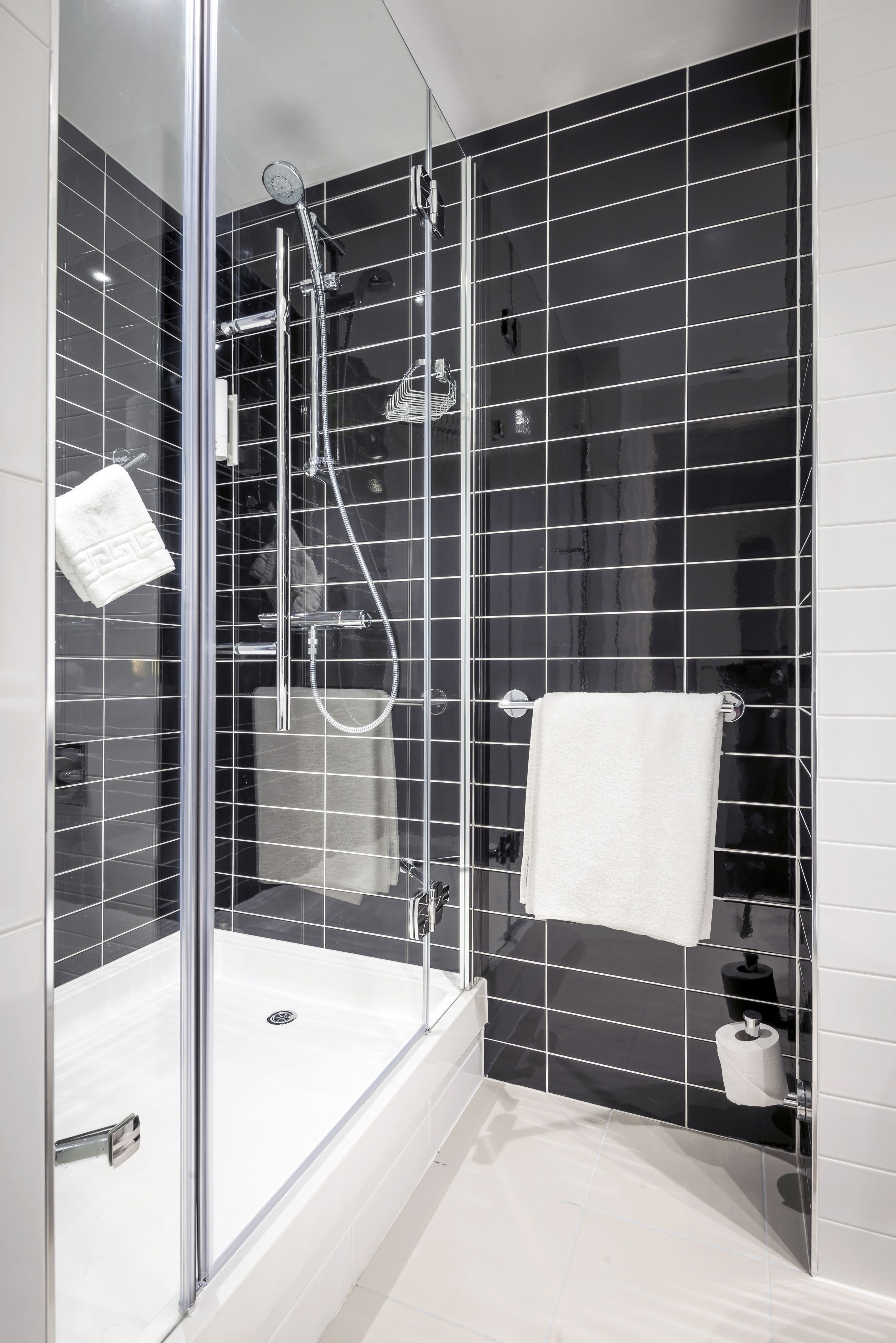 A modern bathroom with a glass-enclosed shower, black tiled walls, and a white bathtub.