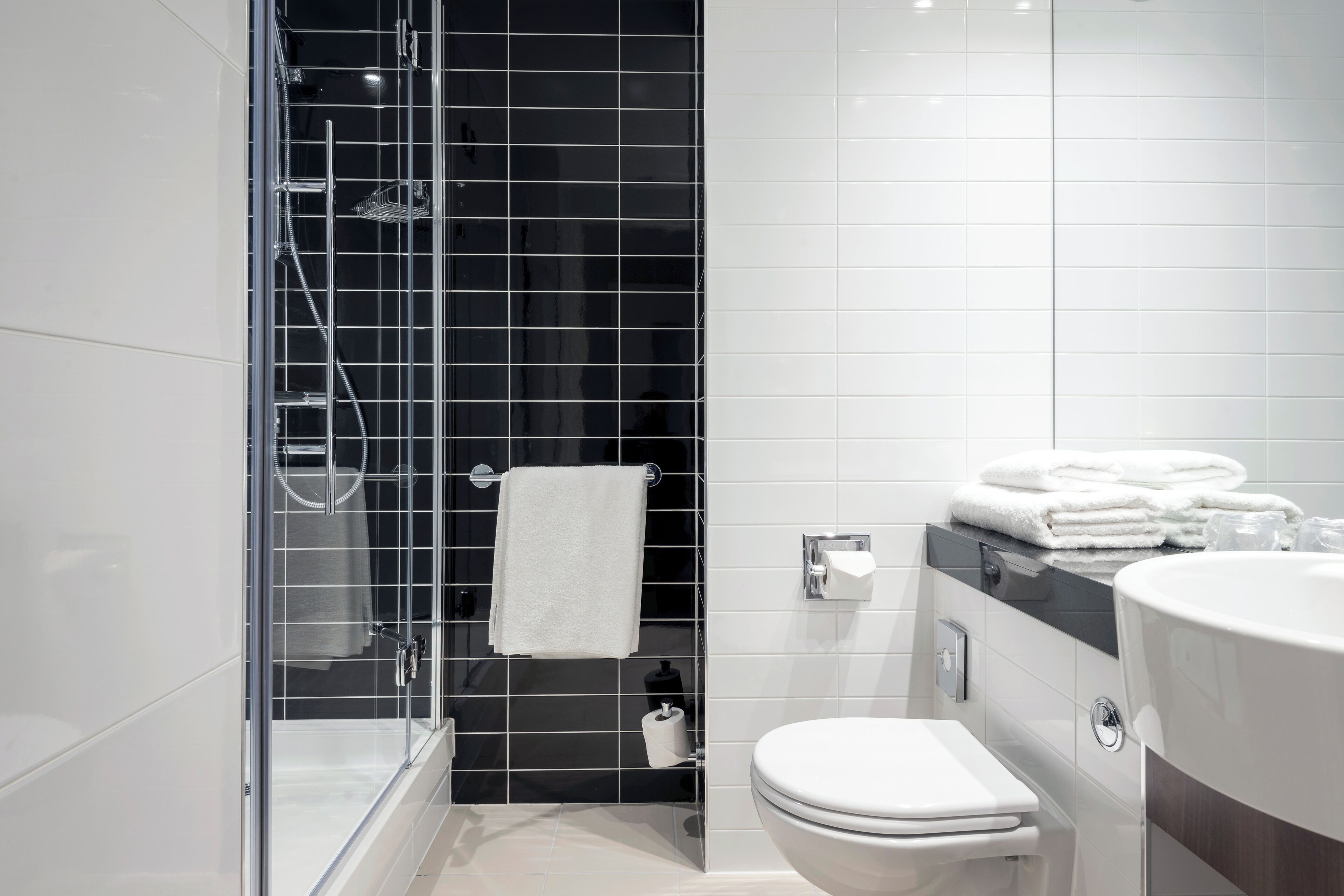 Une salle de bain moderne avec une douche à parois de verre, des toilettes blanches et un meuble-lavabo doté d’un miroir et d’un porte-serviettes.