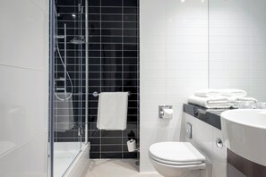 A modern bathroom with a glass-enclosed shower, a white toilet, and a vanity with a mirror and towel rack.