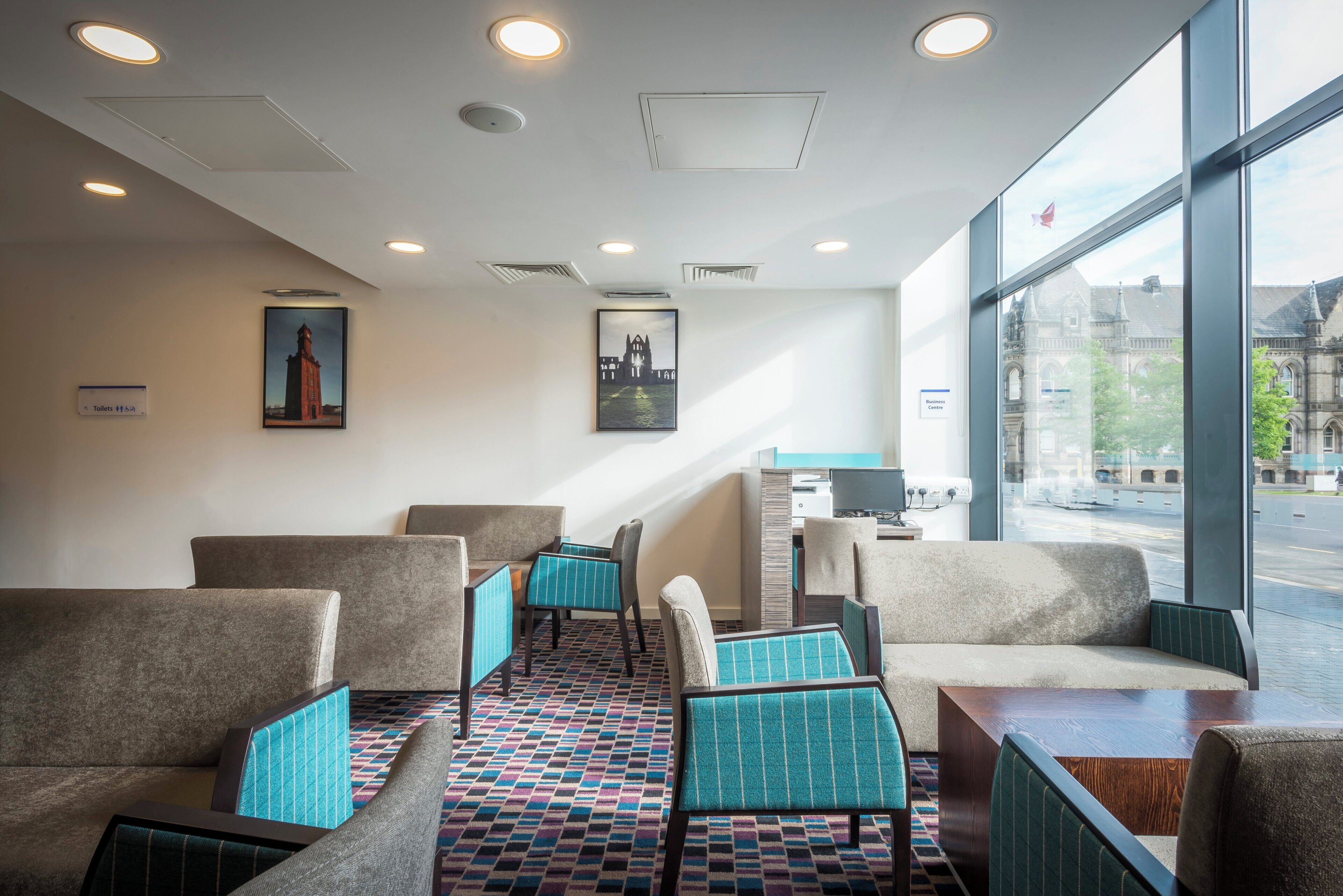 A hotel lobby with seating areas, a reception desk, and large windows offering a view of the city.