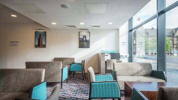 A hotel lobby with seating areas, a reception desk, and large windows offering a view of the city.