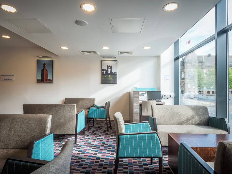A hotel lobby with seating areas, a reception desk, and large windows offering a view of the city.