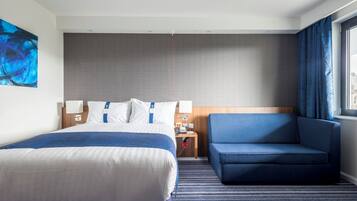 A hotel room with a large bed, a blue sofa, a nightstand with a lamp, and a painting on the wall.