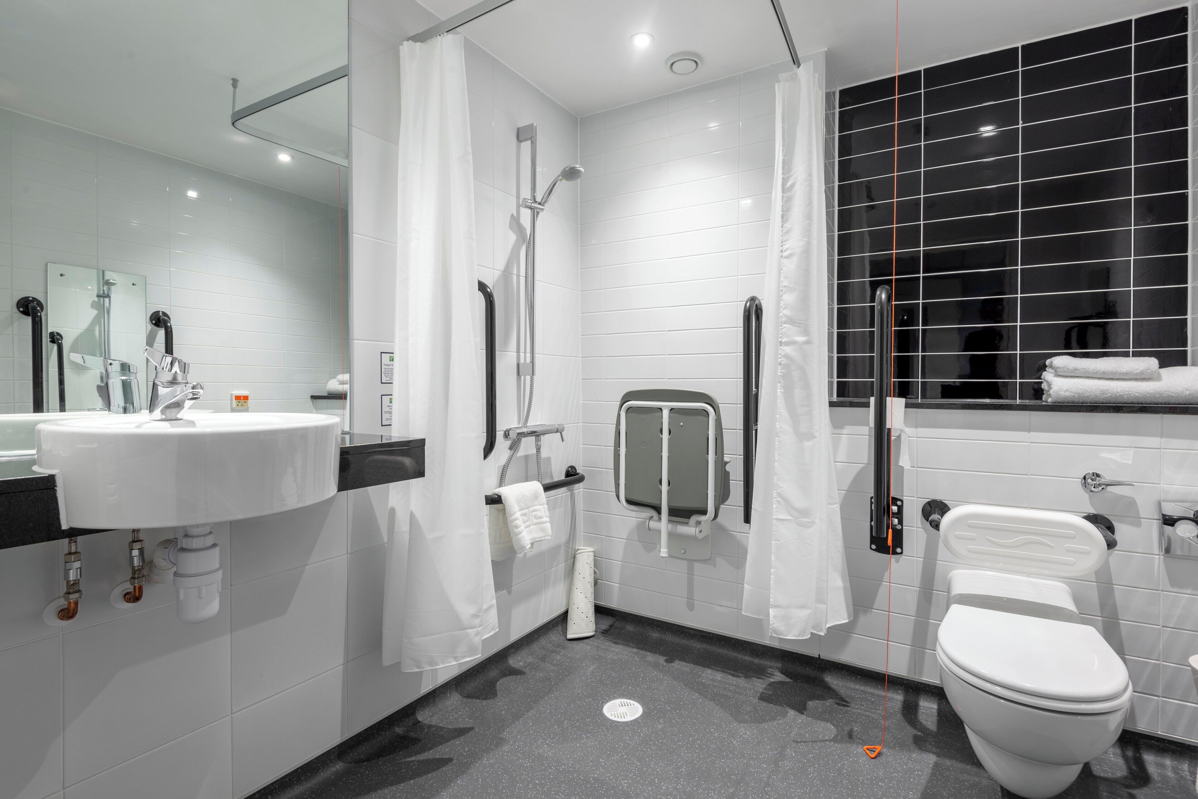 A modern bathroom with a white sink, a toilet, a shower with a glass door, and a black tiled wall.