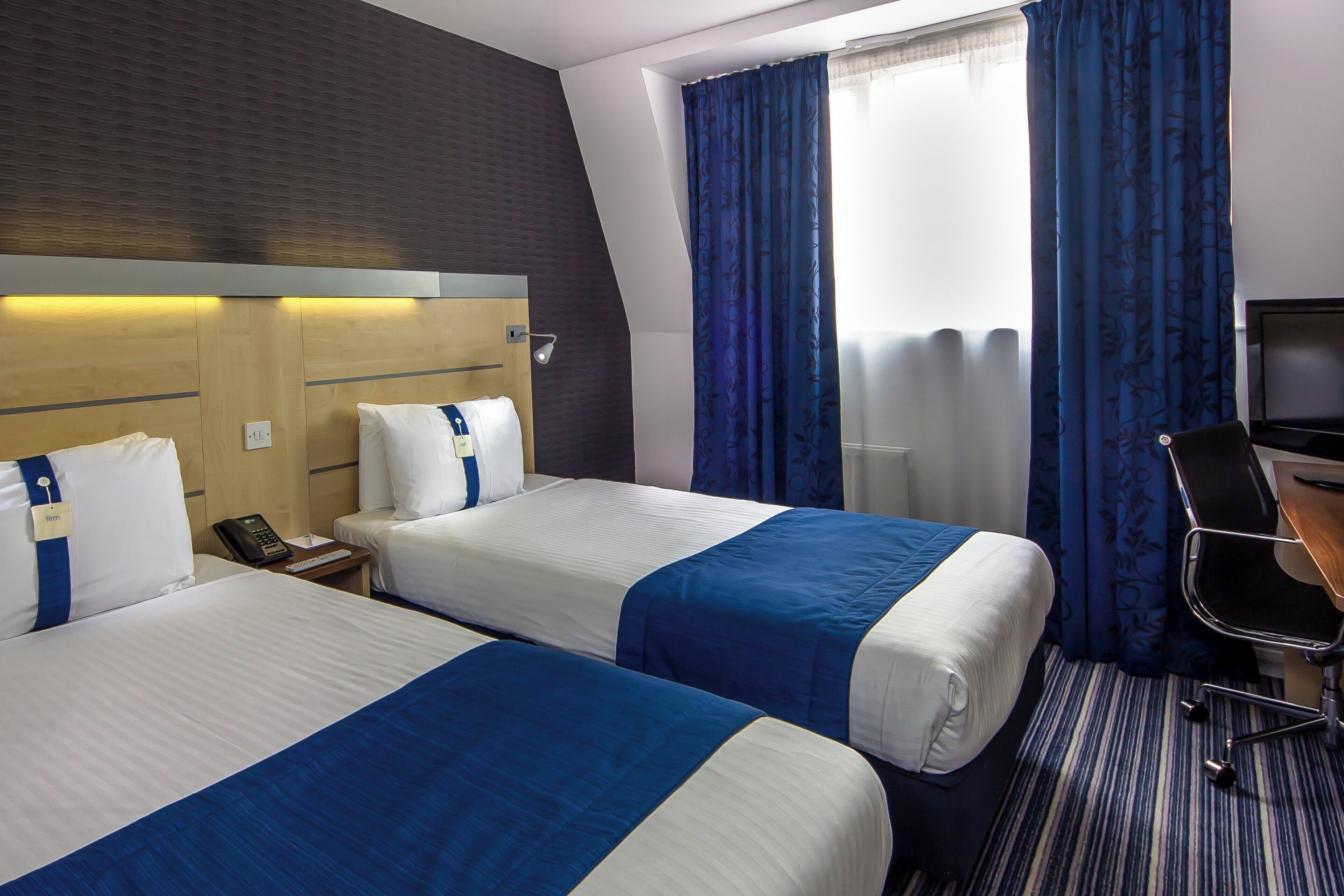 Een hotelkamer met twee bedden, een bureau, een stoel en een televisie.