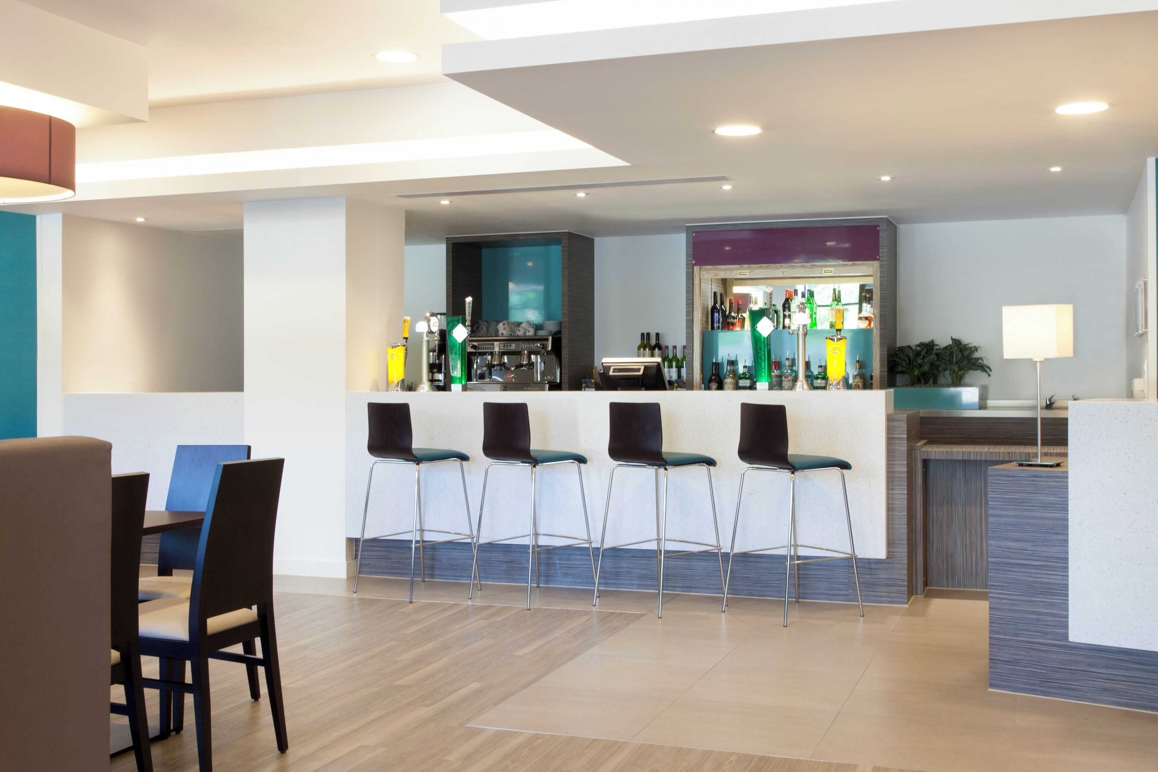 A modern bar area with a counter, bar stools, and a variety of bottles.