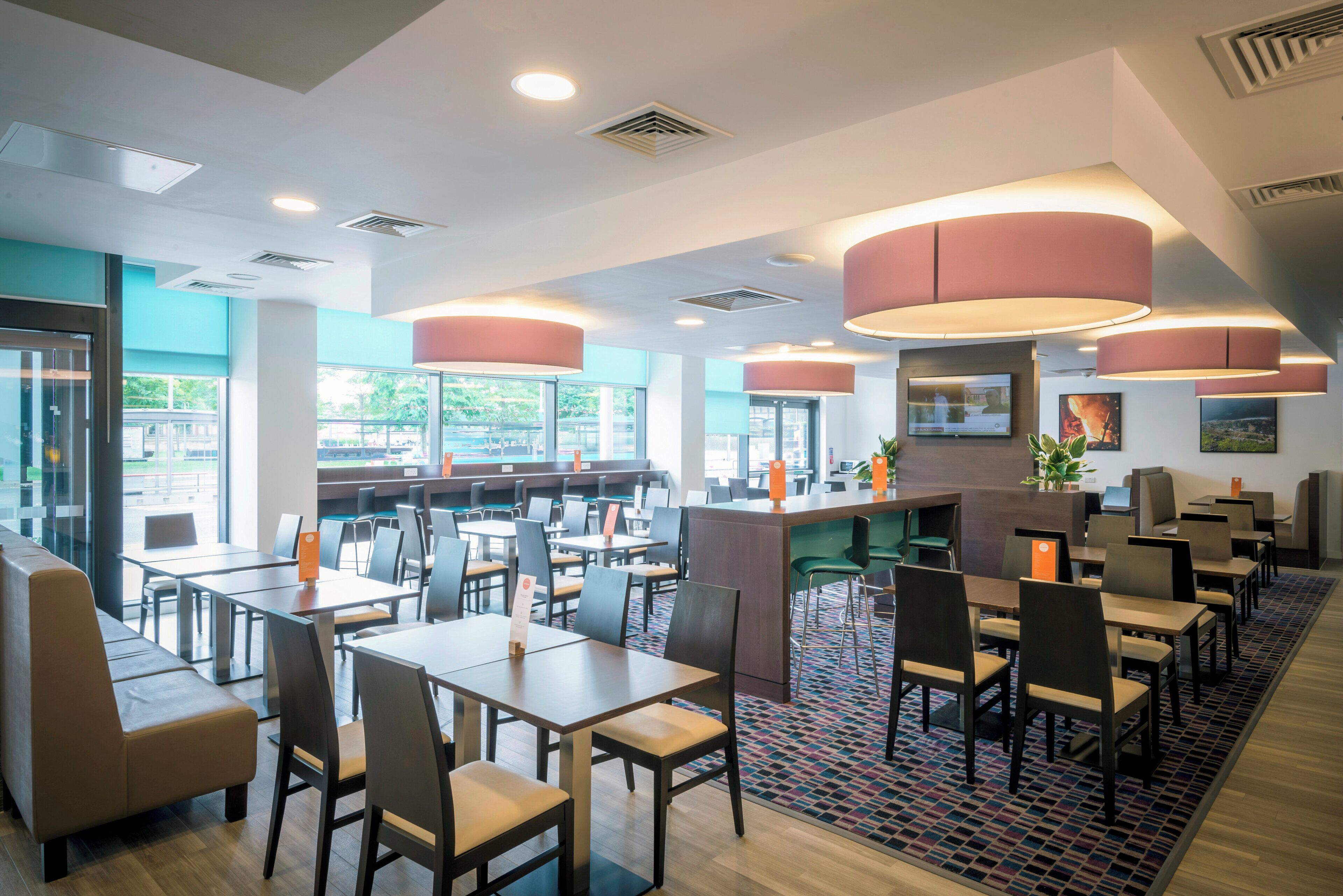 Un interior de restaurante moderno con varias mesas y sillas, ventanas amplias y una zona de barra central.