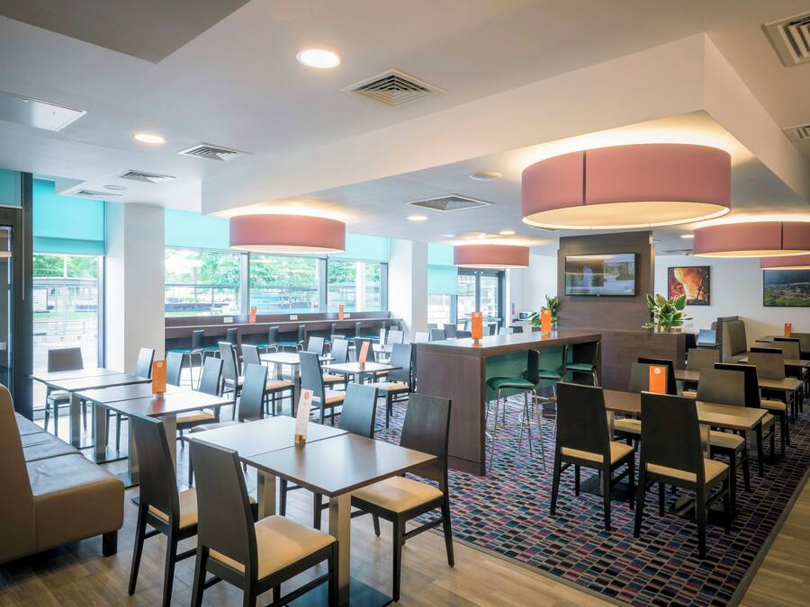 A modern restaurant interior with multiple dining tables and chairs, large windows, and a central counter area.
