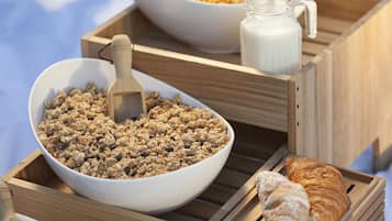 Een ontbijttafel met een kom granola, een croissant en een melkkannetje op houten dienblad.