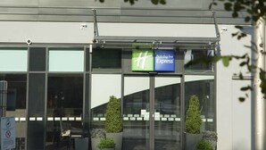 Edificio de Holiday Inn Express con entrada de vidrio, plantas en macetas y una señalización clara sobre las puertas.