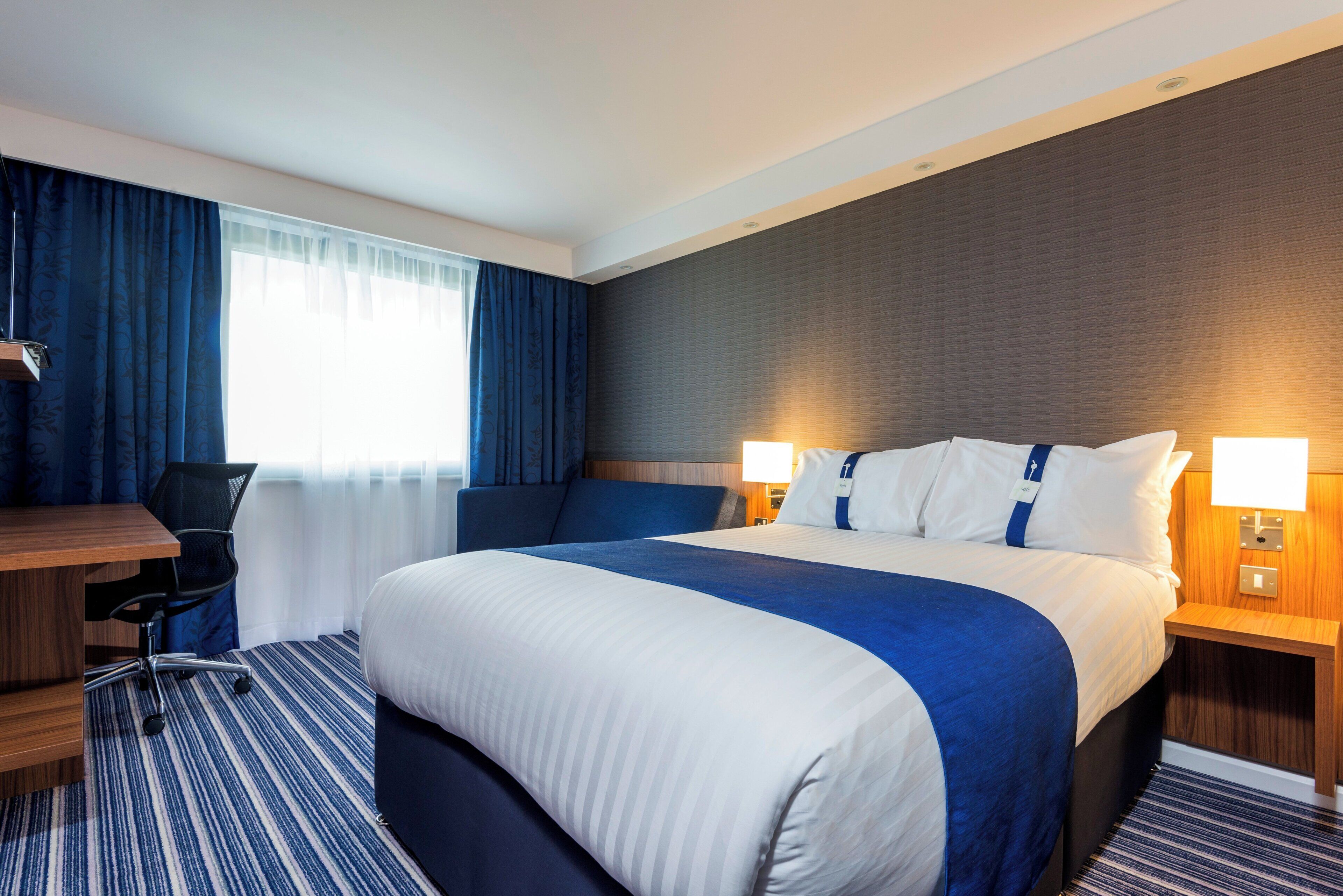 A hotel room with a large bed, a desk, and a chair.