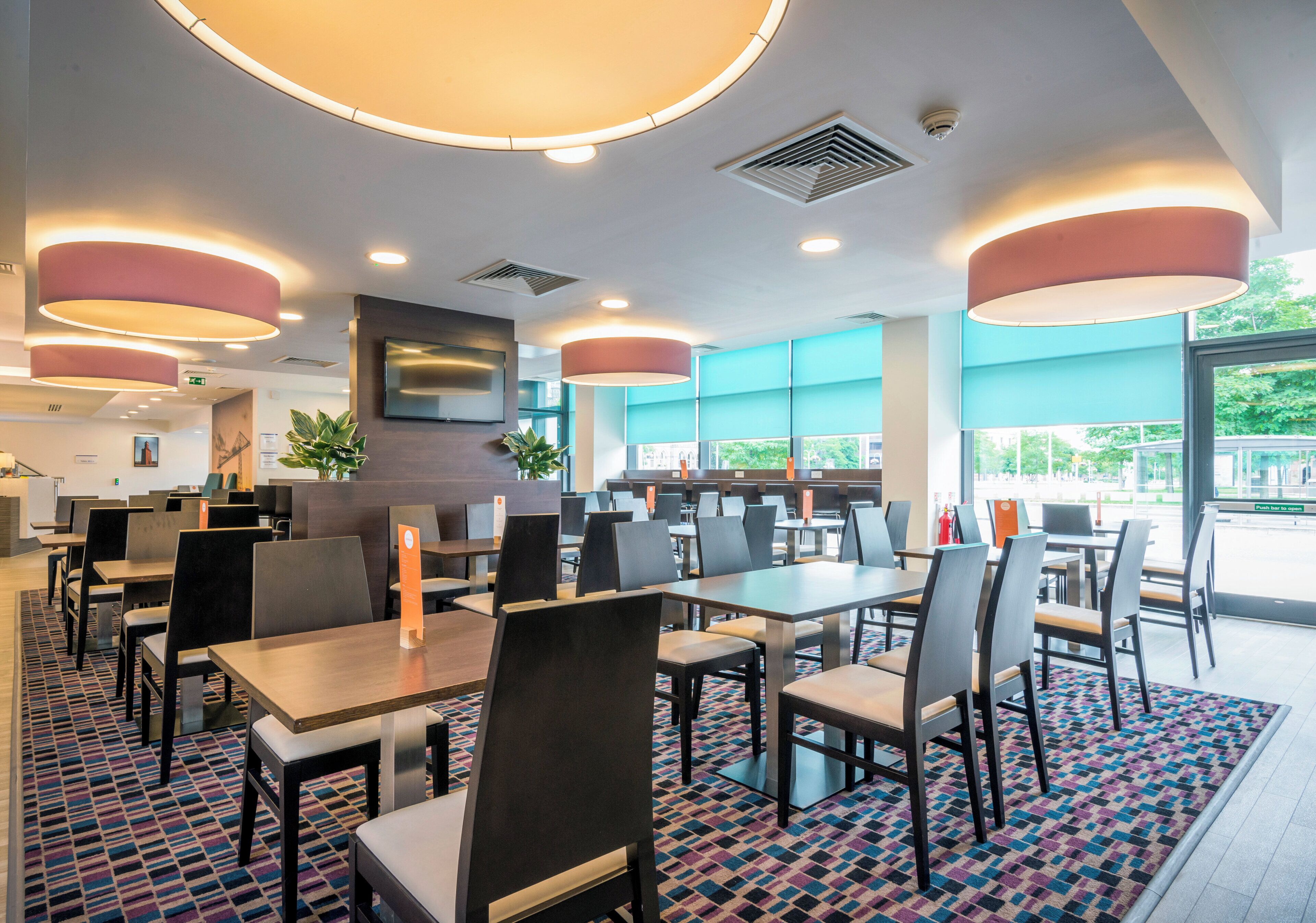 A modern restaurant interior with tables, chairs, and recessed ceiling lighting.