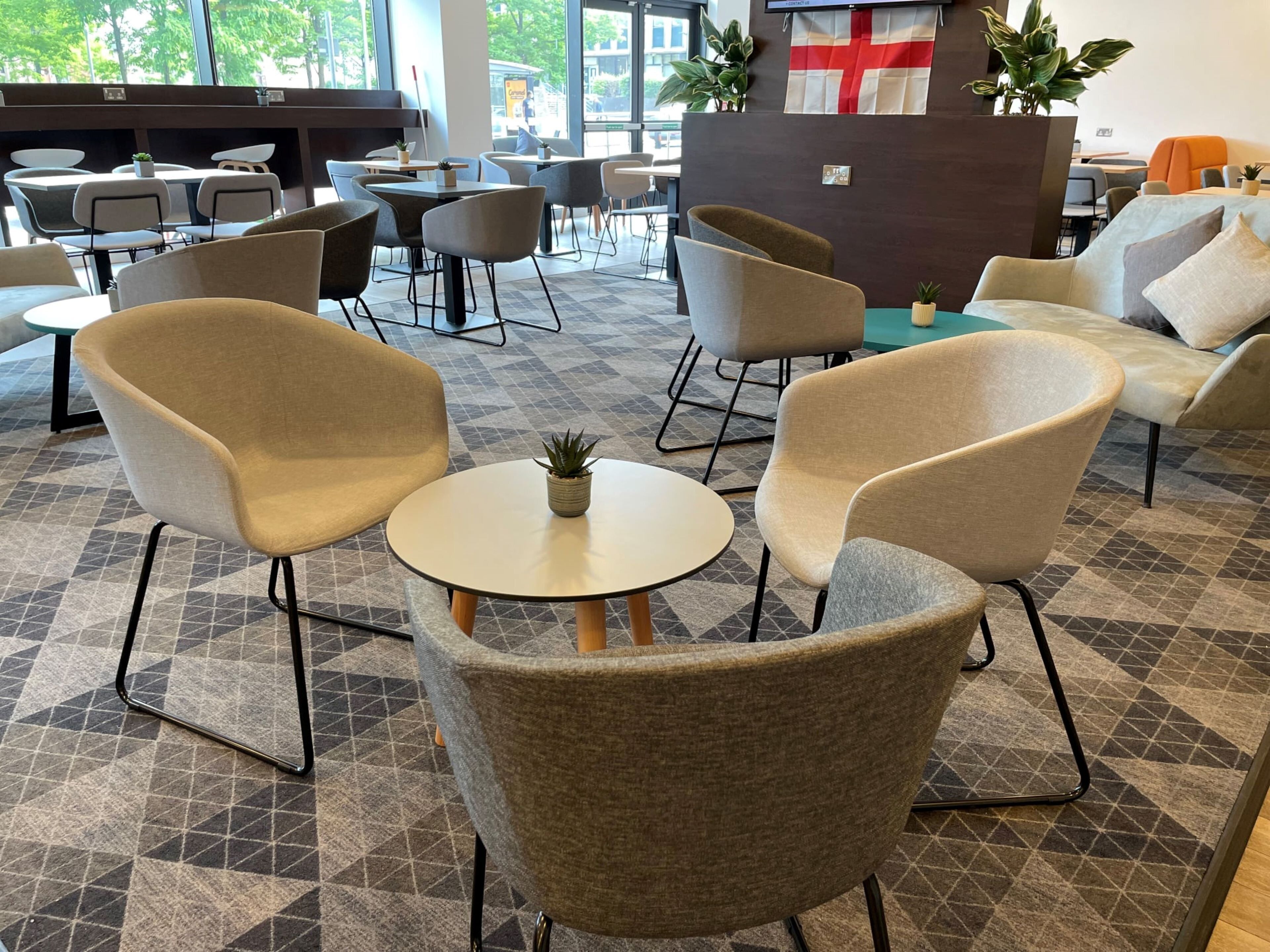 A modern lounge area with round tables and comfortable chairs, a large window offering a view of the outdoors, and a flag on the wall.