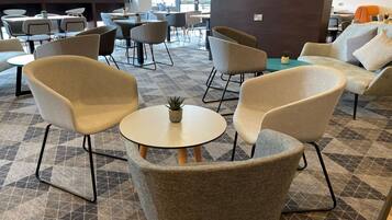 A modern lounge area with round tables and comfortable chairs, a large window offering a view of the outdoors, and a flag on the wall.