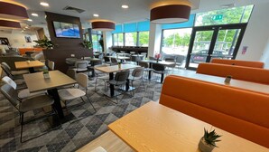 Un restaurante moderno con una mezcla de cabinas y mesas, un televisor de pantalla plana en la pared y grandes ventanales que ofrecen vistas al exterior.