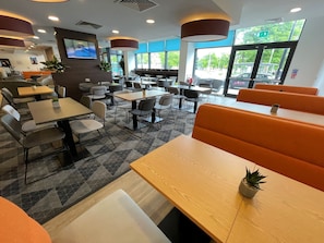 A modern restaurant with a mix of booths and tables, a flat-screen TV mounted on the wall, and large windows offering a view of the outdoors. - Holiday Inn Express Middlesbrough - Centre Square by IHG (Middlesbrough)