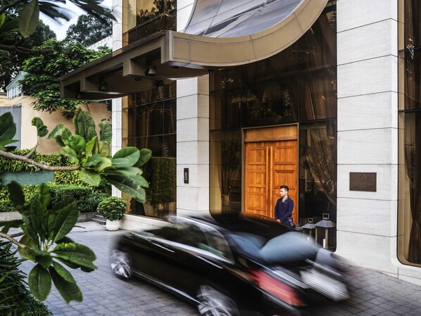 L’entrée moderne d’un hôtel, avec une grande porte en bois, un homme debout près de la porte et une voiture qui passe.