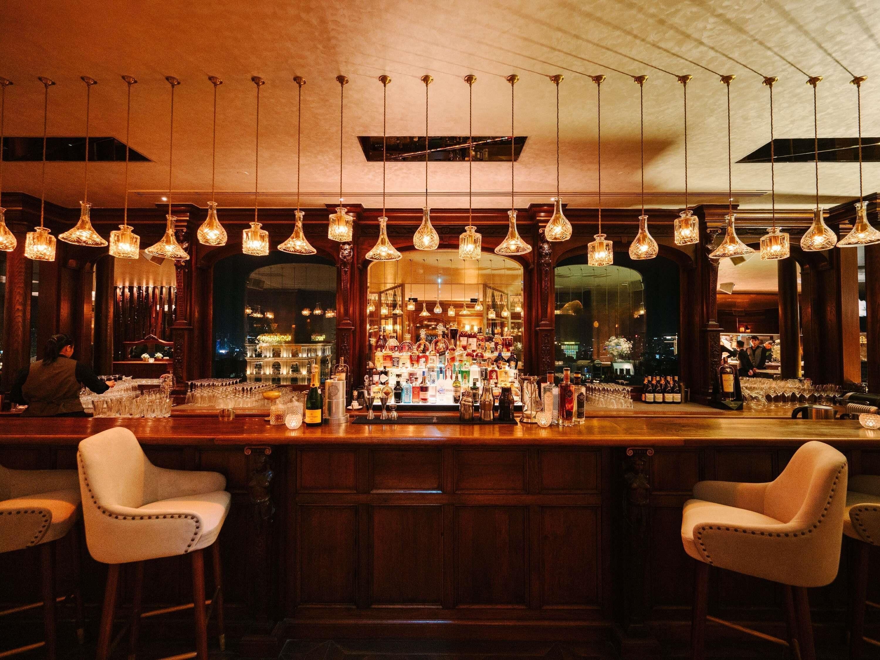 A bar with hanging light fixtures, a bar counter, and two bar stools.