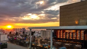 Un bar situé sur le toit d’un immeuble, avec une terrasse et une vue sur la ville au coucher du soleil.