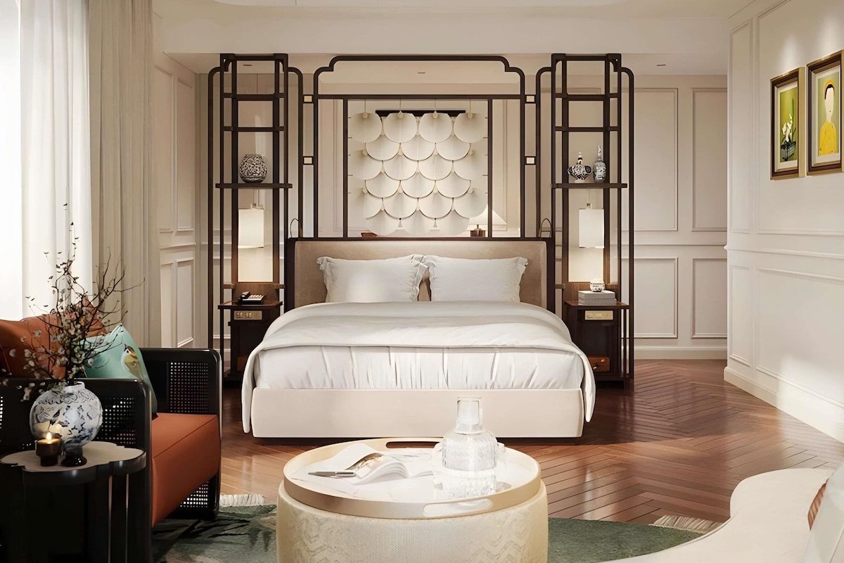Een moderne slaapkamer met een groot bed, een ronde salontafel en een decoratief paneel aan de muur.