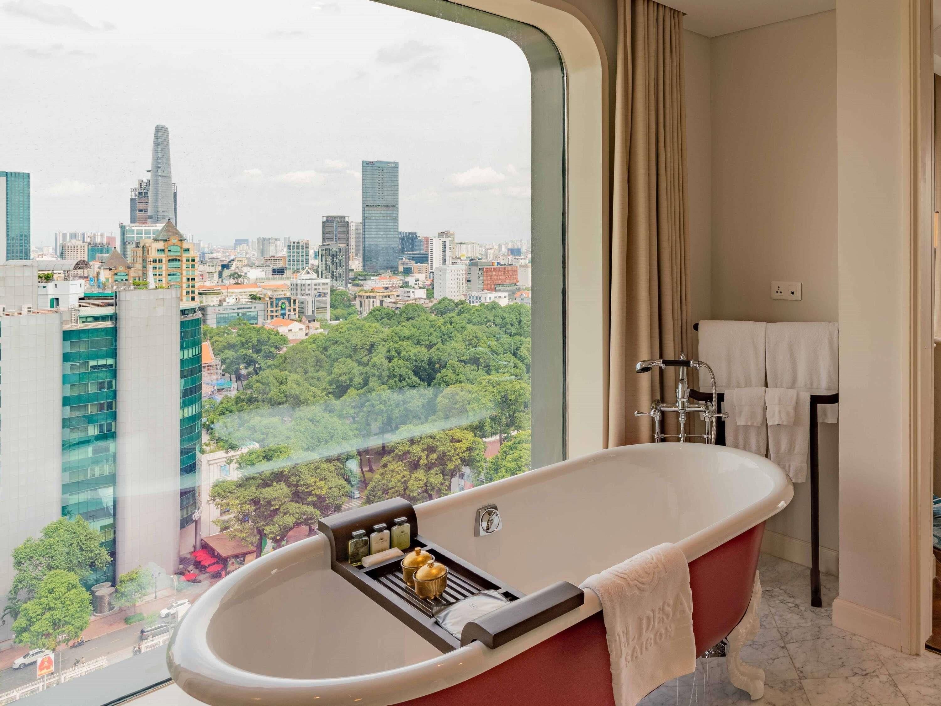 A modern bathroom with a freestanding bathtub, a towel rack, and a window offering a city view.