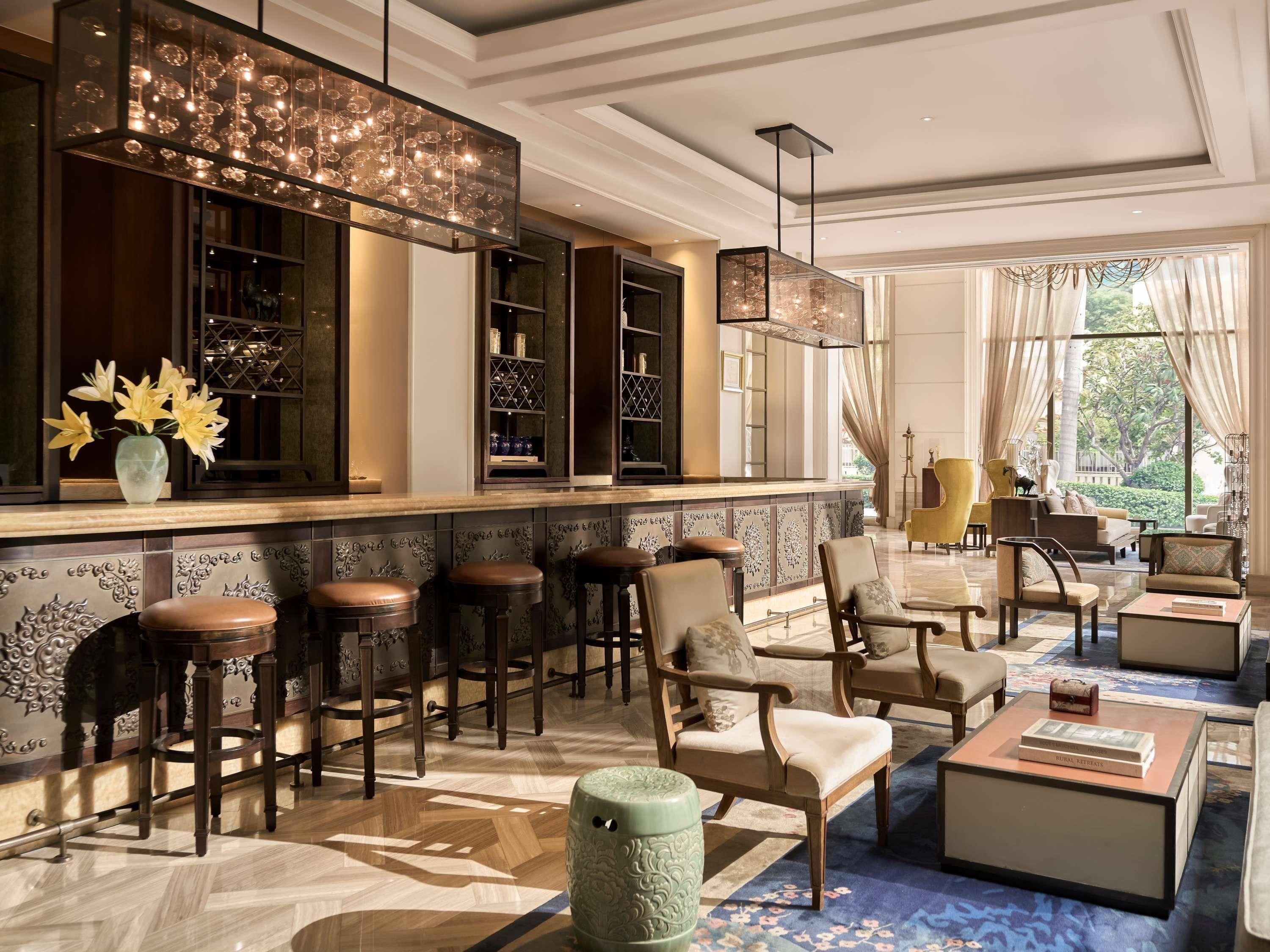 A bar area with stools, a bar counter, and shelves with bottles. There are chairs and a sofa in the seating area.
