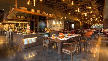 A modern restaurant with a central bar area, multiple dining tables, and a polished floor.